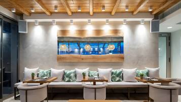 A modern lounge area with a wooden ceiling, a large wall-mounted artwork, and a seating arrangement with tables and chairs.