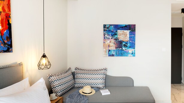 Una habitación de hotel moderna con cama, sofá, mesita de noche, un sombrero y un cuadro en la pared.
