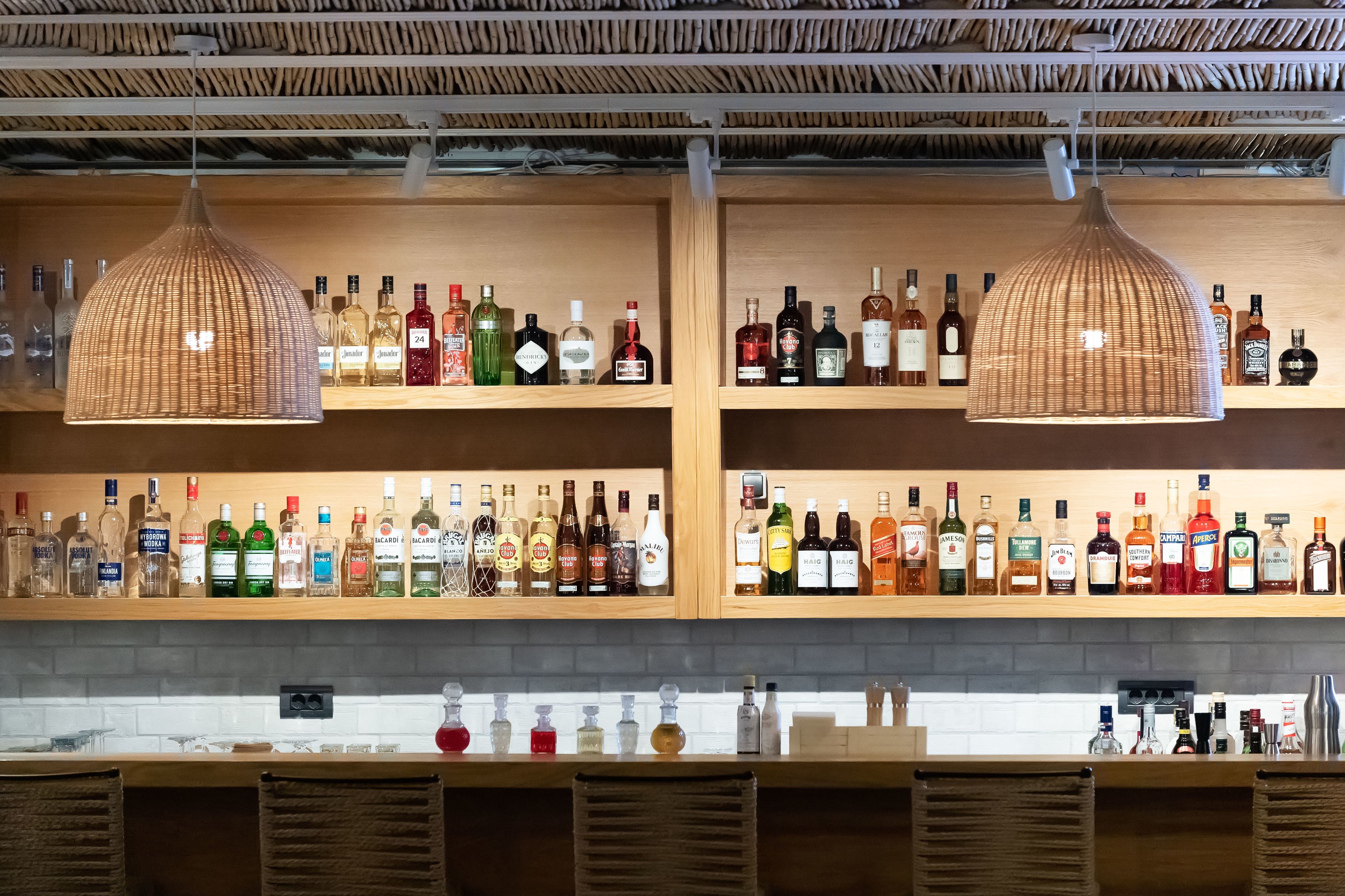 En bar med flere hylder fyldt med flasker spiritus og en bardisk med barudstyr.