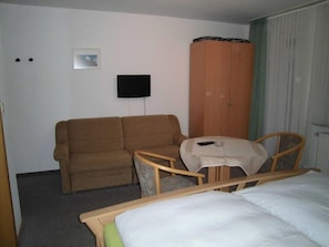 Una camera d'albergo con un letto, un divano, un tavolino, una televisione e un armadio.
