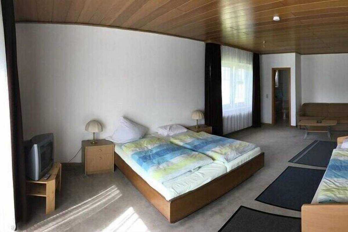 A bedroom with a large bed, a smaller bed, a desk, a chair, and a television.