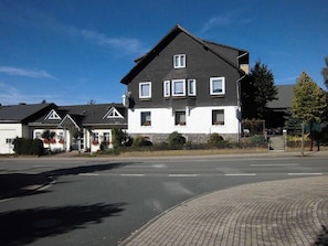 Un edificio residenziale a due piani con tetto scuro e pareti bianche, caratterizzato da numerose finestre e un ingresso frontale ben visibile.