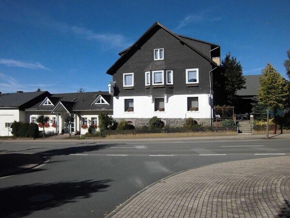 A two-story residential building with a dark roof and white walls, featuring multiple windows and a visible front entrance.