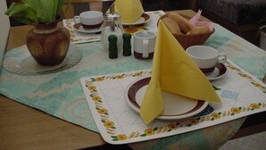 Una mesa de comedor con mantel floral, un jarrón con flores, saleros y pimenteros, una cesta de pan y servilletas dobladas en triángulos.