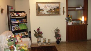 Una habitación con un mostrador de recepción de madera, una estantería con revistas, un cuadro enmarco y varios jarrones con flores.