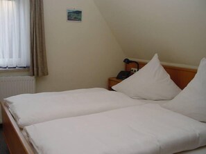 A hotel room with two single beds, a nightstand with a lamp, and a window with curtains. - Pension und Landhaus Wölfel (Bad Steben)