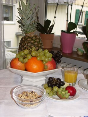 A fruit platter with a pineapple, oranges, grapes, and a glass of orange juice on a table. - Pension und Landhaus Wölfel (Bad Steben)