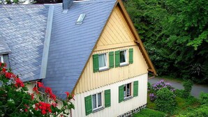Una casa de dos pisos con techo inclinado, contraventanas verdes y cimientos de piedra.