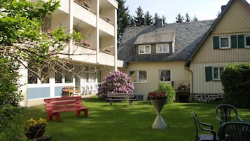 A courtyard with a red bench, a table, and chairs. There is a building with balconies and a flower pot with pink flowers.