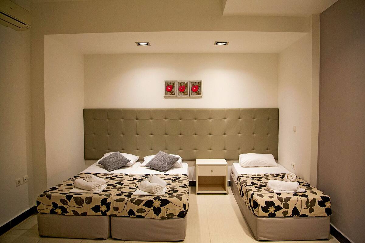 A hotel room with two beds, a headboard, a nightstand, and a wall-mounted artwork.