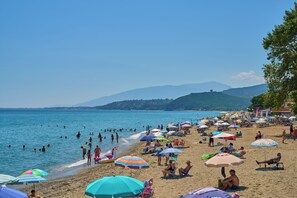 Una spiaggia affollata con persone che nuotano e prendono il sole sotto ombrelloni colorati.