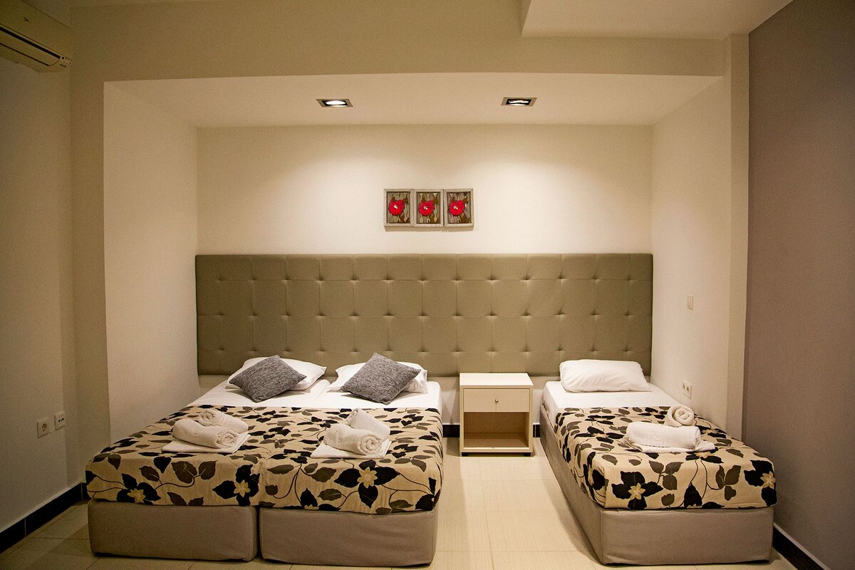 A hotel room with two beds, a headboard, a nightstand, and a wall-mounted artwork.
