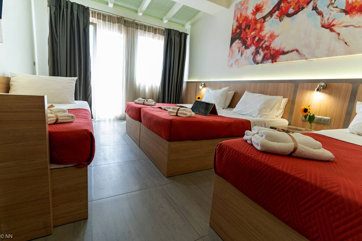 A hotel room with two single beds, a sofa bed, a desk with a laptop, and a large painting on the wall.