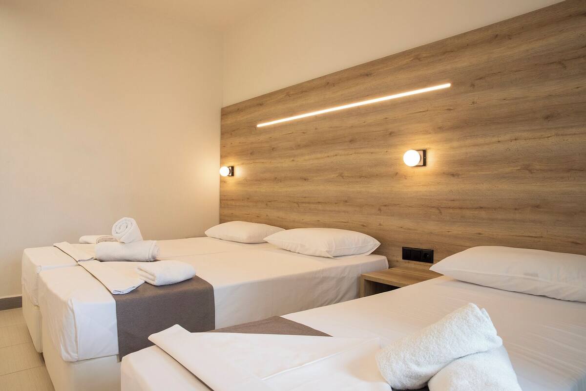 A hotel room with two beds, each with white linens and towels, a wooden headboard, and wall-mounted lights.