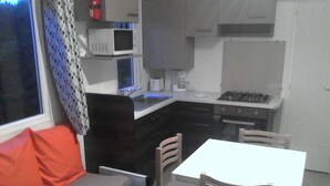 Cocina compacta con microondas, estufa y pileta. Pequeño comedor con mesa y sillas.