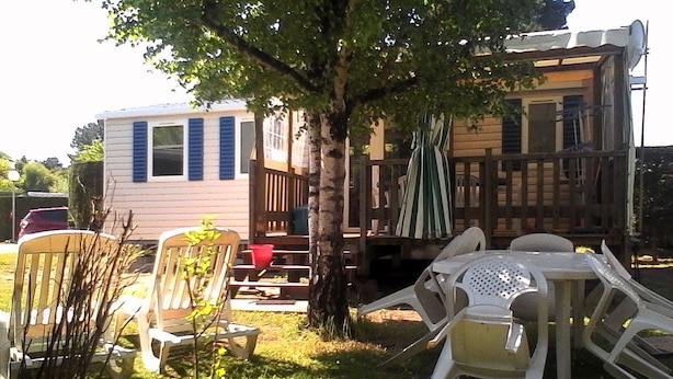 Un patio trasero con una terraza de madera, una silla blanca, una mesita y un árbol.