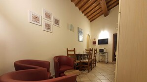 A dining area with red chairs, a wooden table, and a tiled floor. There are framed pictures on the wall and a microwave on a cart.