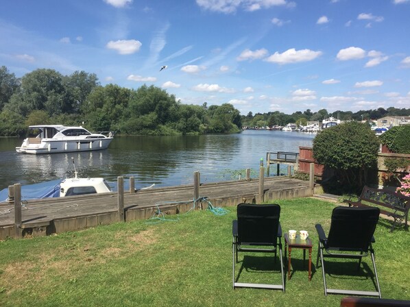 Vista del río con un muelle, un bote y dos sillas de jardín.