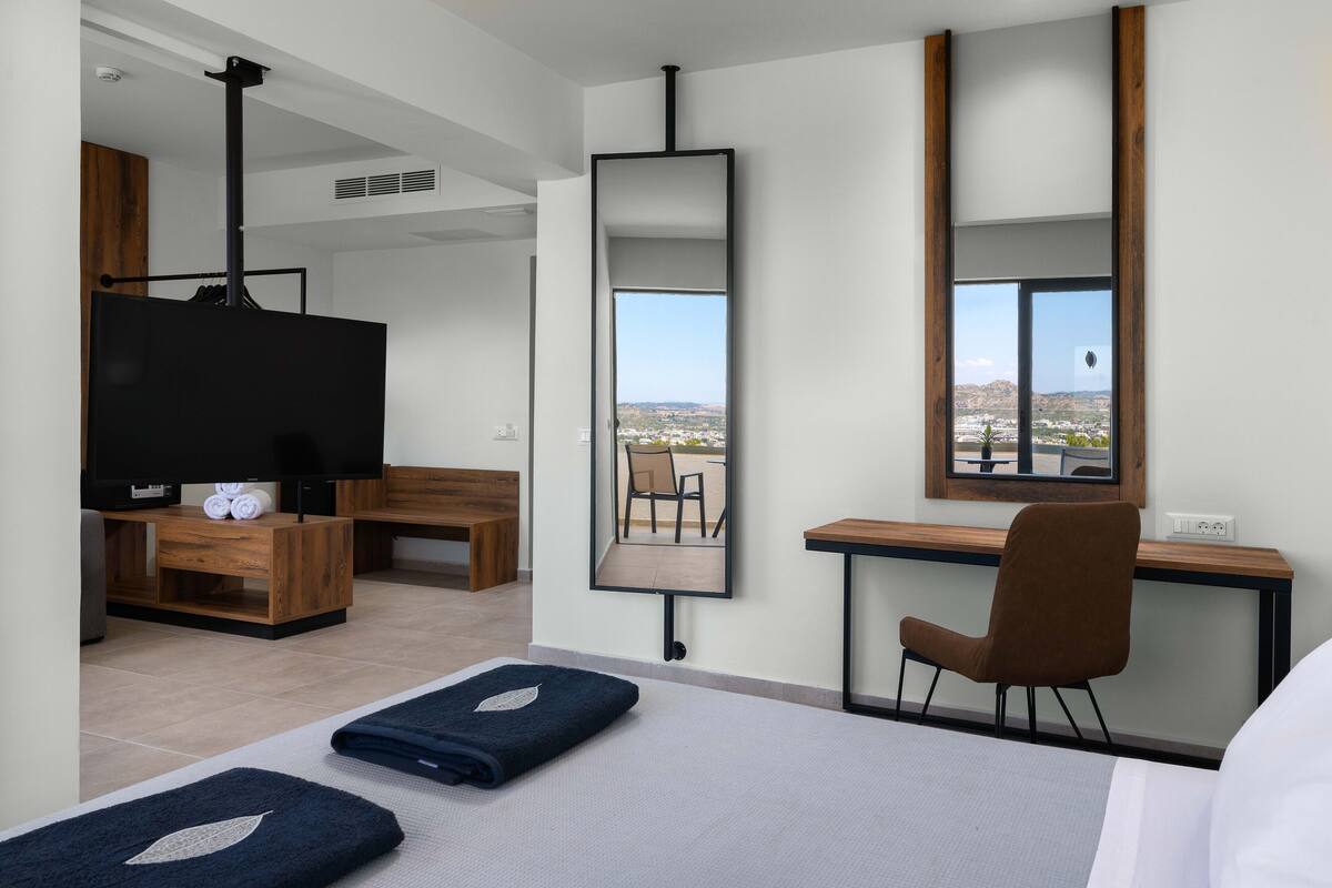 Une chambre d’hôtel moderne équipée d’un lit, d’un bureau, d’une chaise, d’une télévision et d’une grande fenêtre donnant sur la ville.