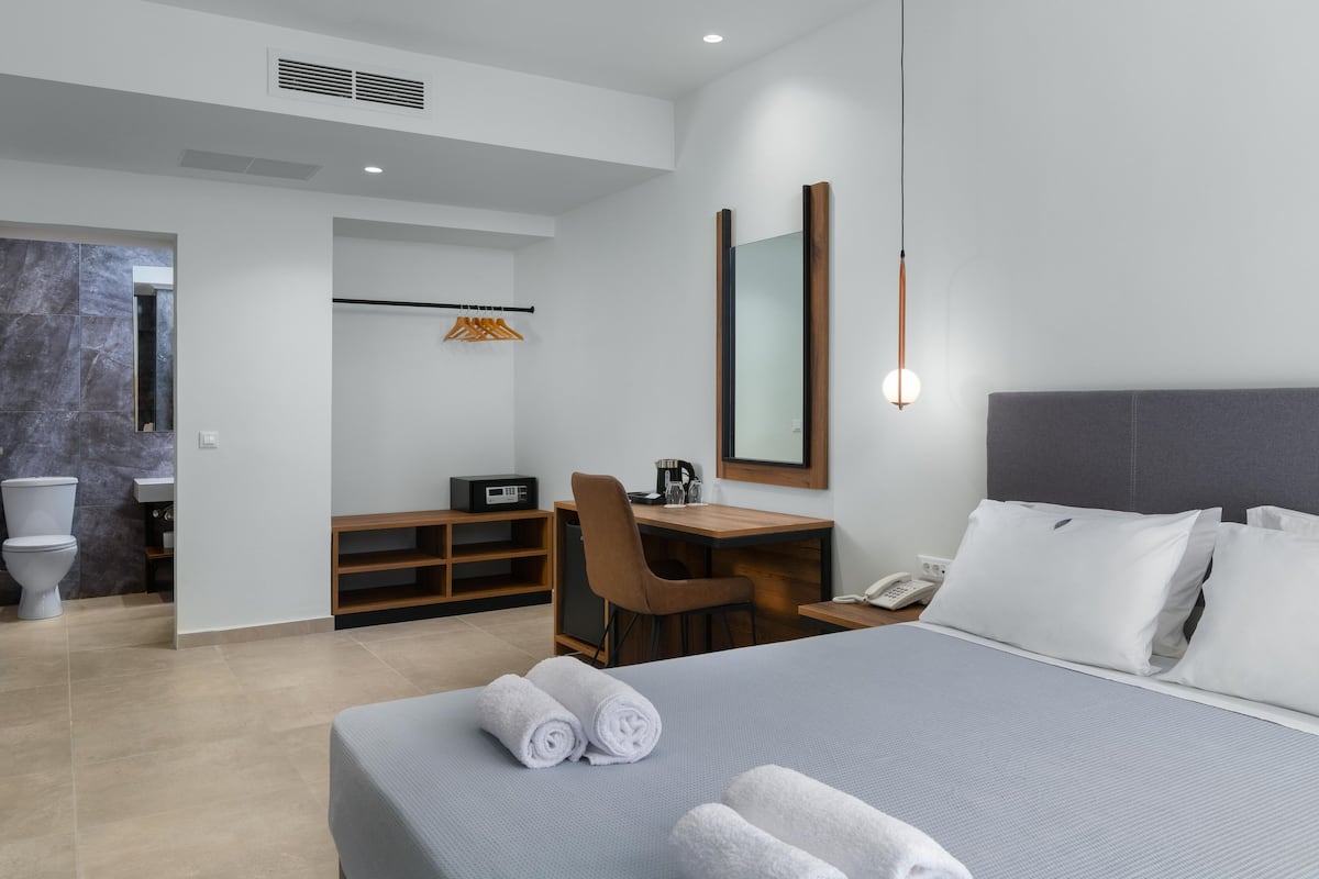 Une chambre d’hôtel moderne équipée d’un grand lit, d’un bureau, d’une chaise, d’un miroir, d’un téléphone et d’une salle de bain avec des toilettes et un lavabo.