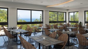 Un restaurante con amplios ventanales que ofrecen vistas al océano, sillas de mimbre y mesas modernas.