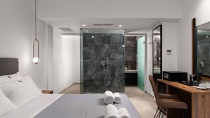 Una habitación de hotel moderna con una cama grande, un escritorio con silla, zona de ducha y baño.