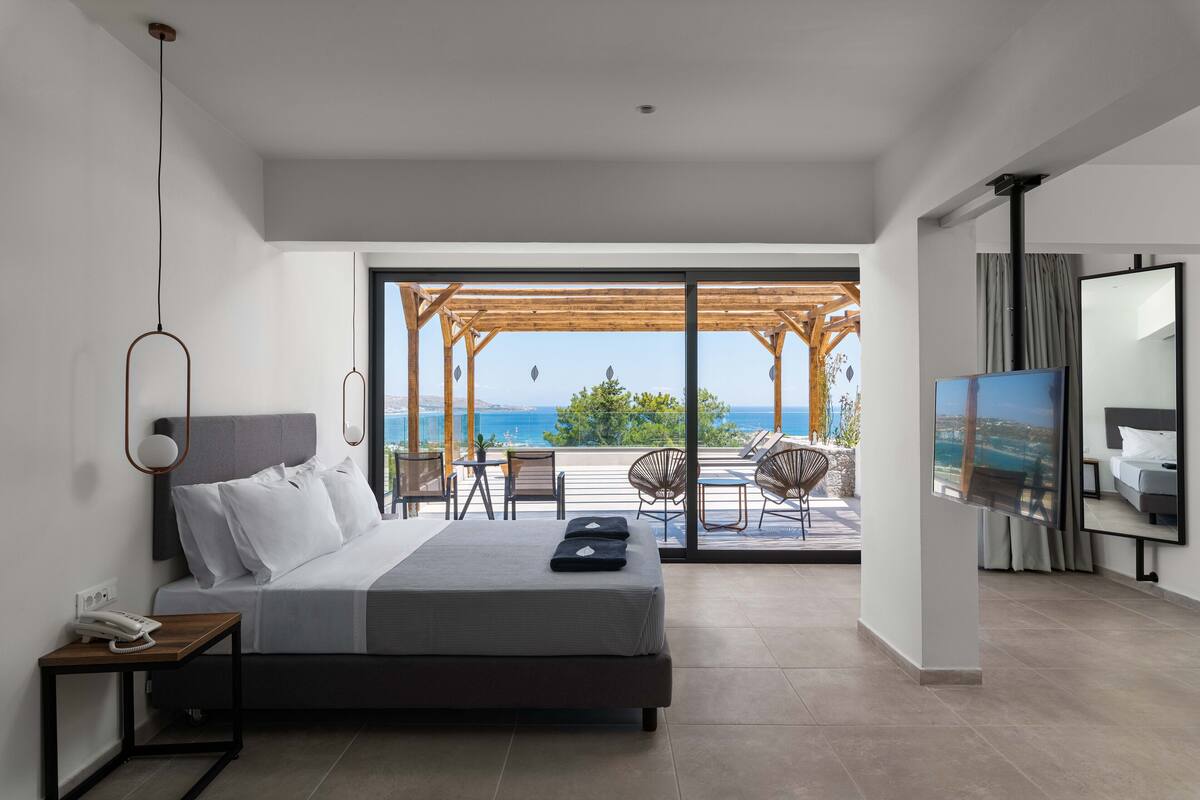 Une chambre moderne avec un lit, une télévision et un balcon aménagé avec du mobilier d’extérieur.