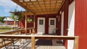 A red building with a wooden porch, a white door, and a small table with chairs.