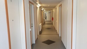 A hotel corridor with doors on both sides, a fire extinguisher on the right wall, and a clock on the wall.