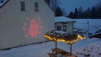 Un bâtiment sur lequel est projetée une image du Père Noël, avec un toit enneigé et un banc décoré de guirlandes lumineuses.