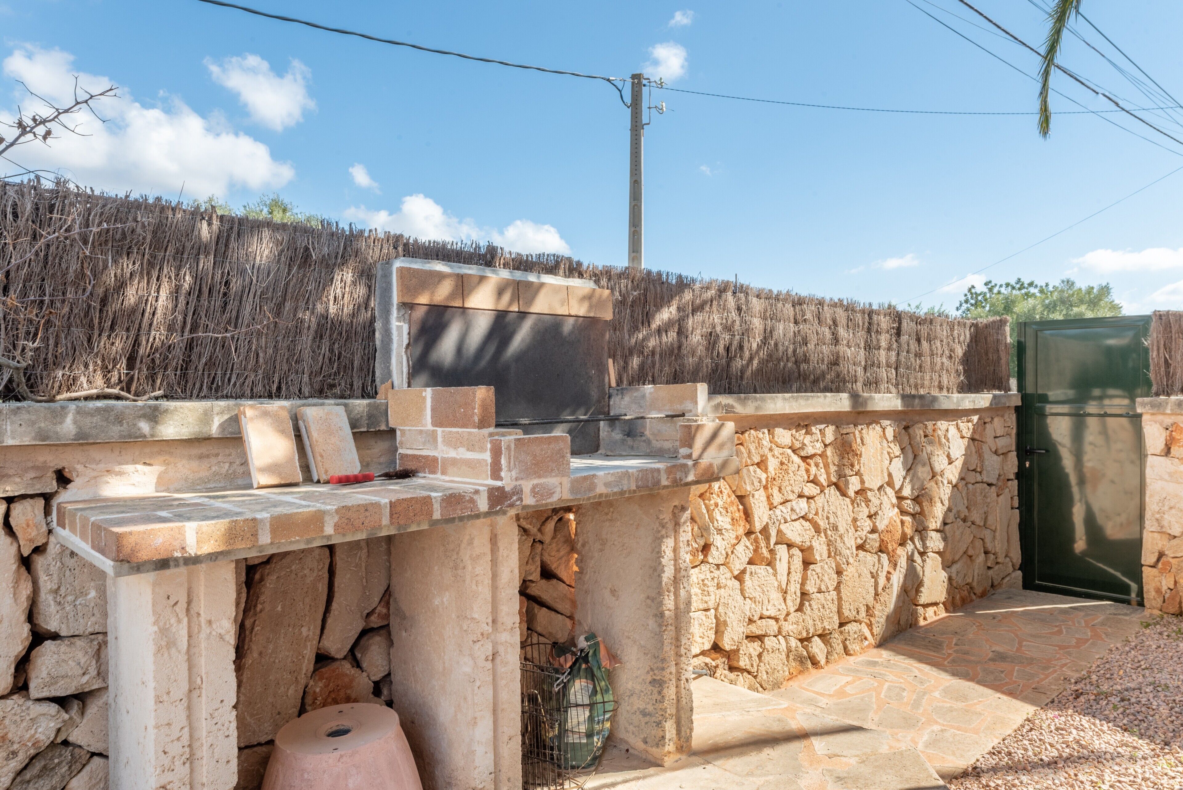 Cocina de exterior de piedra con pared de piedra, una puerta verde y cielo despejado.
