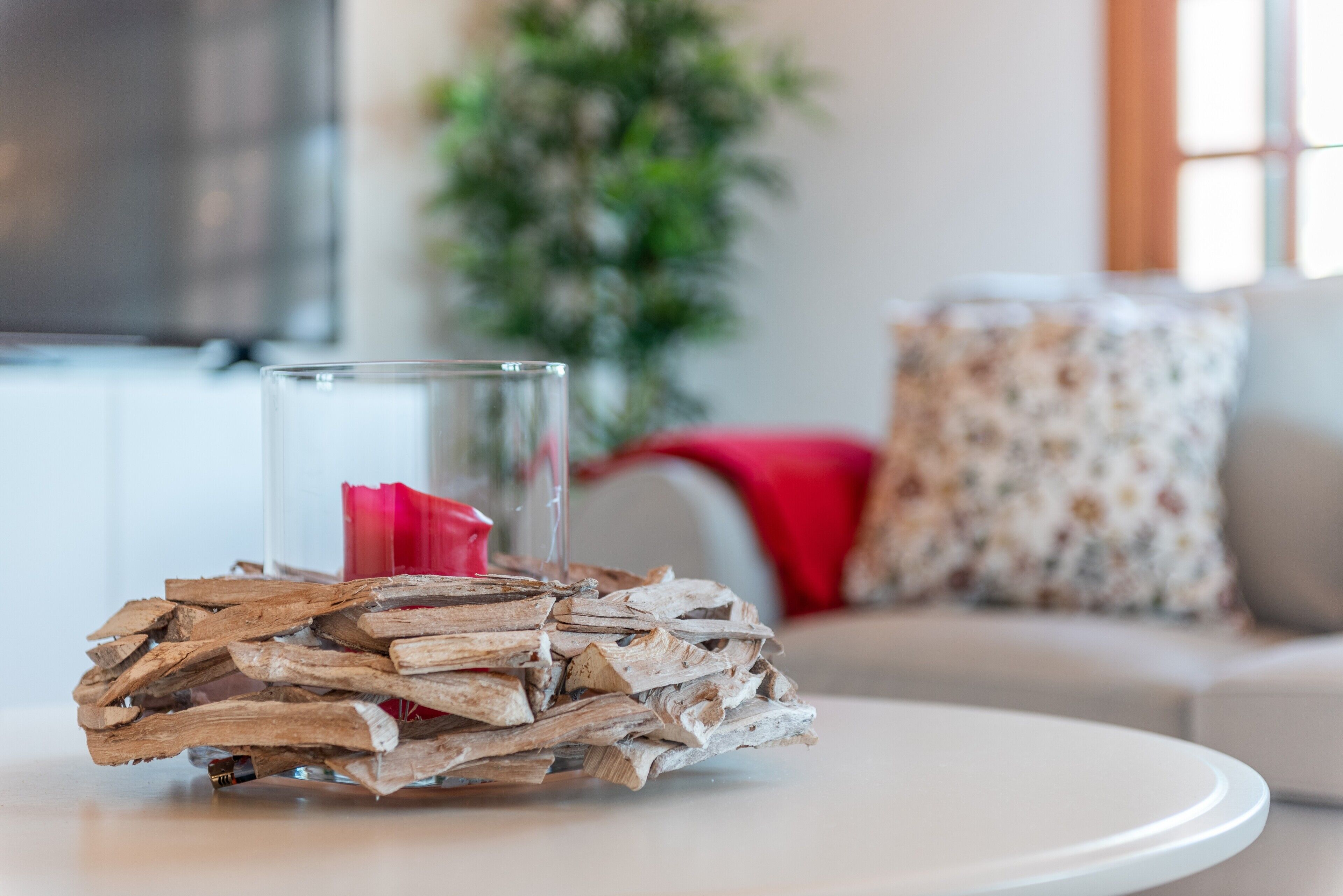 Un vase en verre avec une fleur rouge, posé sur un socle en bois, sur une table blanche.