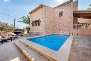Un edificio in pietra con piscina, lettini e una zona coperta.