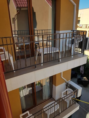 Ein mehrstöckiges Gebäude mit einem Balkon im zweiten Stock, der mit Gartenmöbeln und einem Geländer ausgestattet ist.