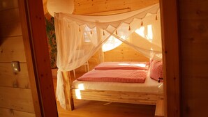 A wooden cabin bedroom with a bed under a canopy, a bedside table, and a wall-mounted light switch. - Fantastic apartment in a log cabin in front of the mountains (Wielenbach)