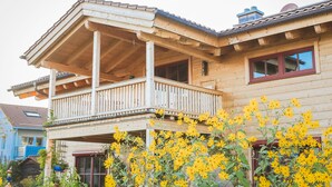A wooden house with a balcony and a garden with yellow flowers. - Fantastic apartment in a log cabin in front of the mountains (Wielenbach)