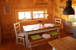 A wooden cabin interior with a dining table, chairs, a bench, and a lamp.