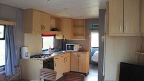 A compact kitchen with wooden cabinets, a microwave, a stove, and a sink. There is a dining area with a table and chairs.