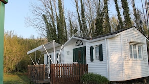 A small white cabin with a wooden deck and a fenced area.