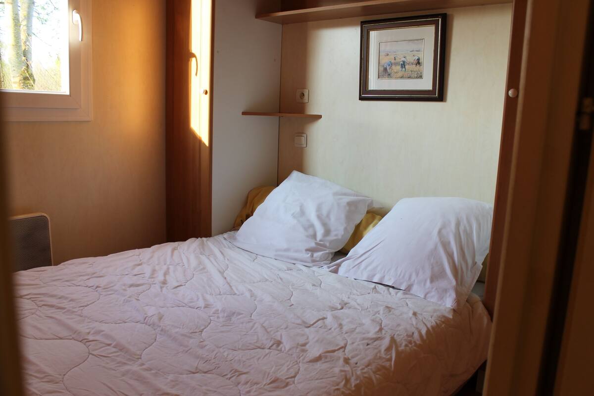 Un dormitorio con cama, ropa de cama blanca, cabecero, ventana y un cuadro en la pared.