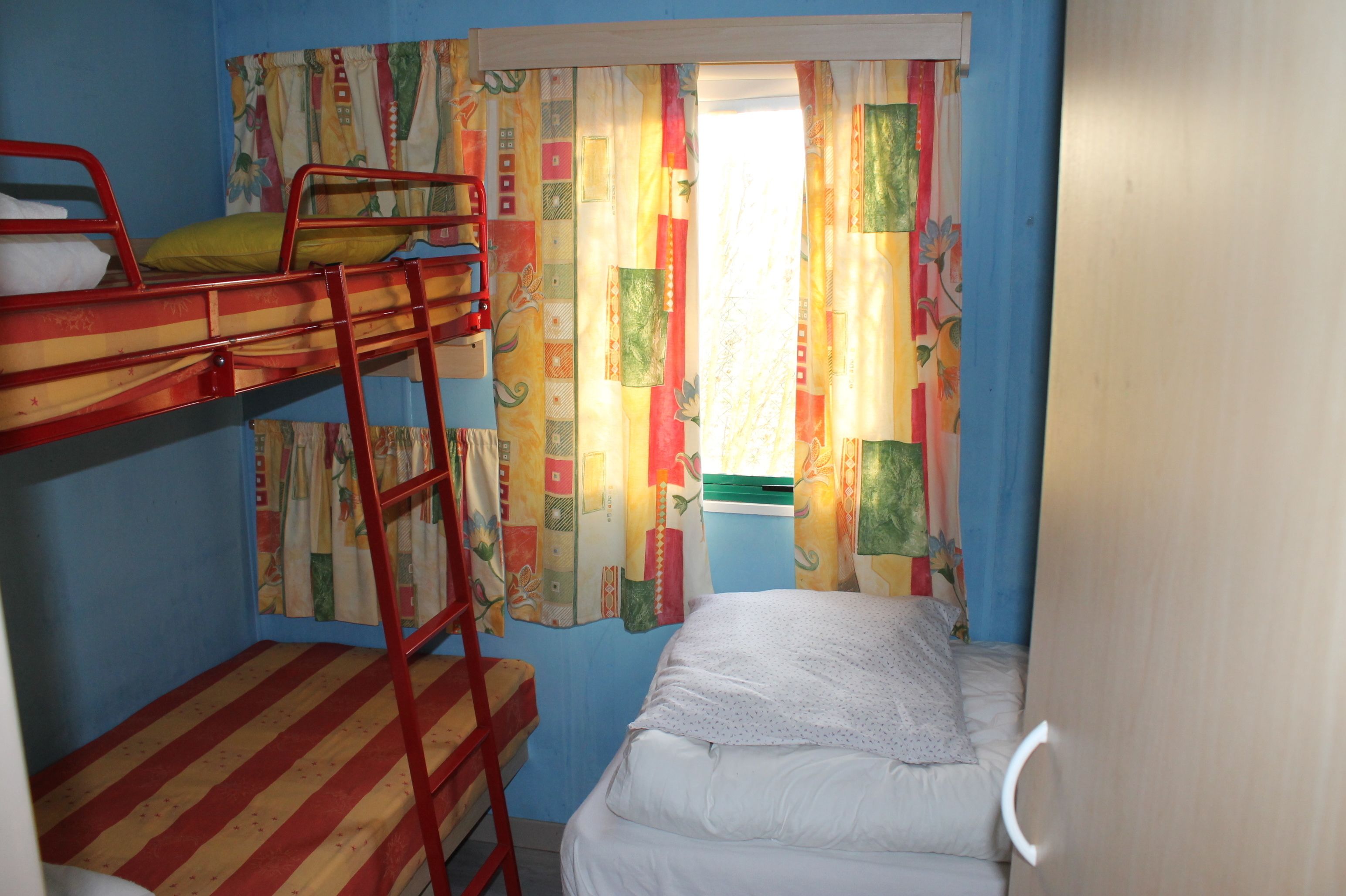 A bunk bed room with a ladder, a window with colorful curtains, and a single bed.
