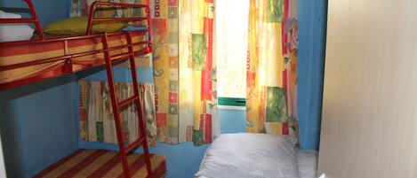 A bunk bed room with a ladder, a window with colorful curtains, and a single bed.