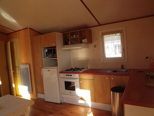 Una cocina compacta con armarios de madera, microondas, refrigerador, estufa y lavaplatos.