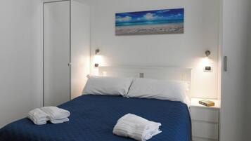 A neatly made bed with white linens, a blue bedspread, and two bedside lamps.