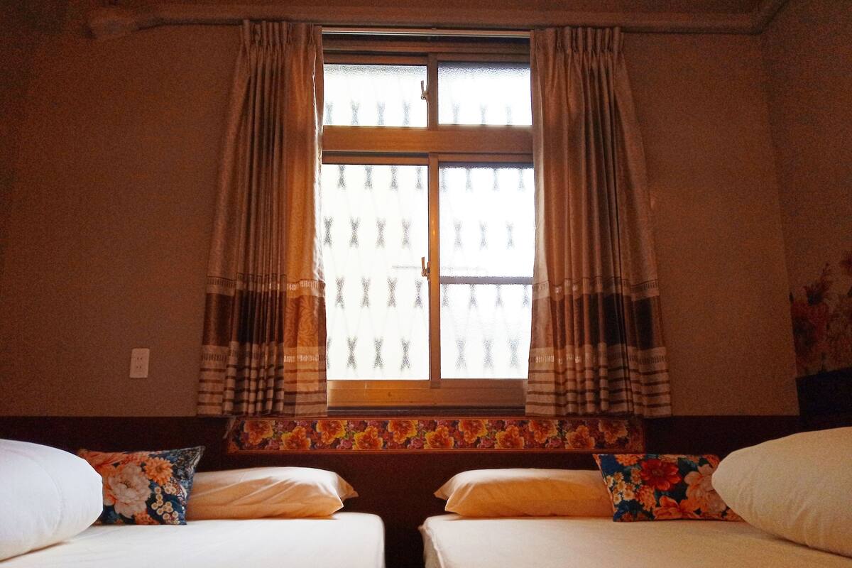 A room with two beds, a window with curtains, and a floral-patterned headboard.
