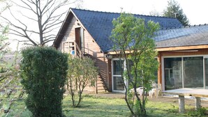 Een houten chalet met een schuin dak, een grote schuifdeur en een klein terras met een bankje.