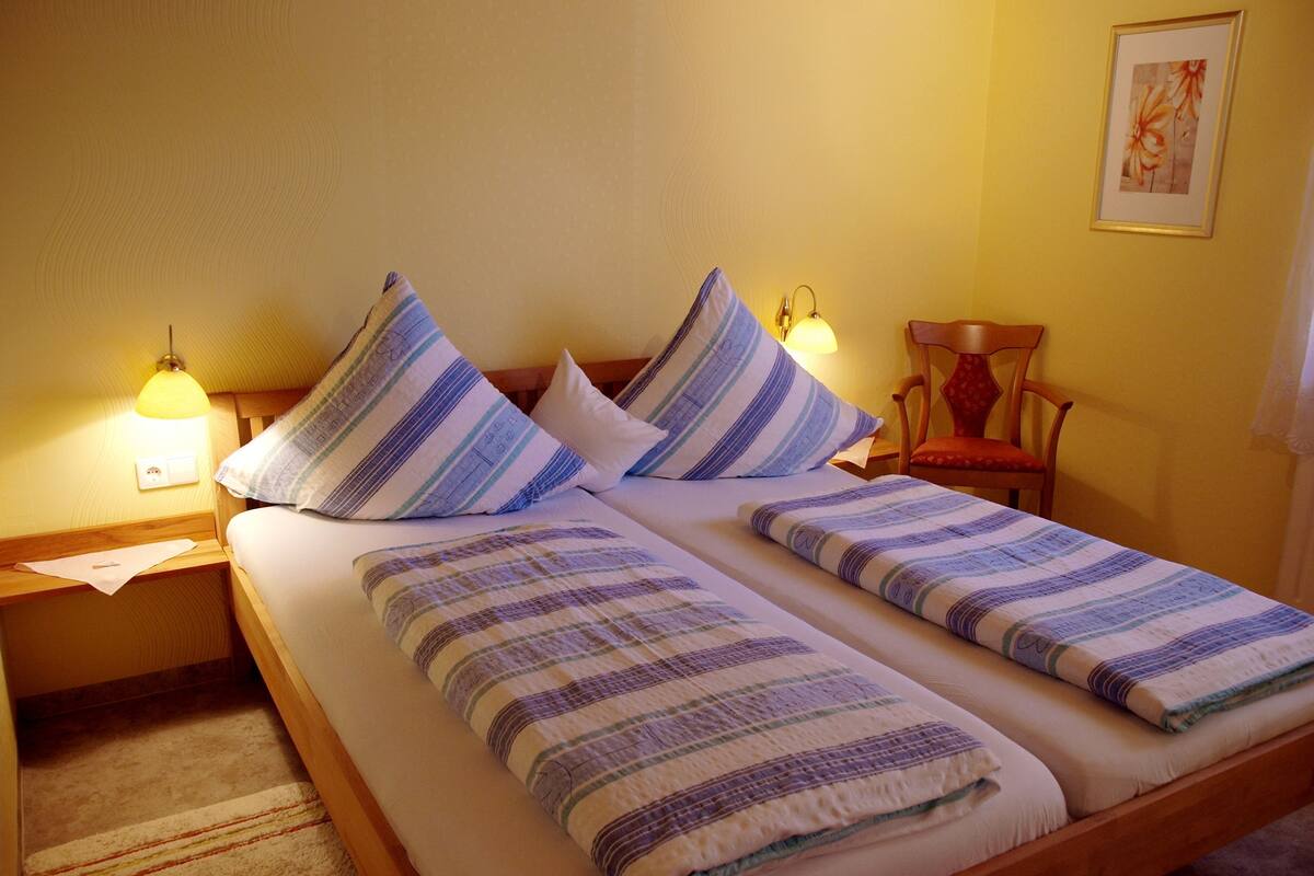 Una cama doble con ropa de cama a rayas, dos lámparas de noche, una silla e imagen colgada en la pared.