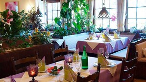 Un restaurante con mesas dispuestas para comer, rodeado de abundante vegetación interior y luz natural que entra por amplias ventanas.