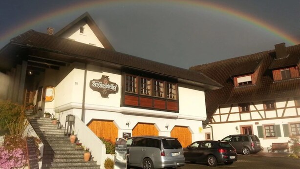 Un edificio con un cartel que dice "Der Ginsberghof" y un arcoíris en el cielo.