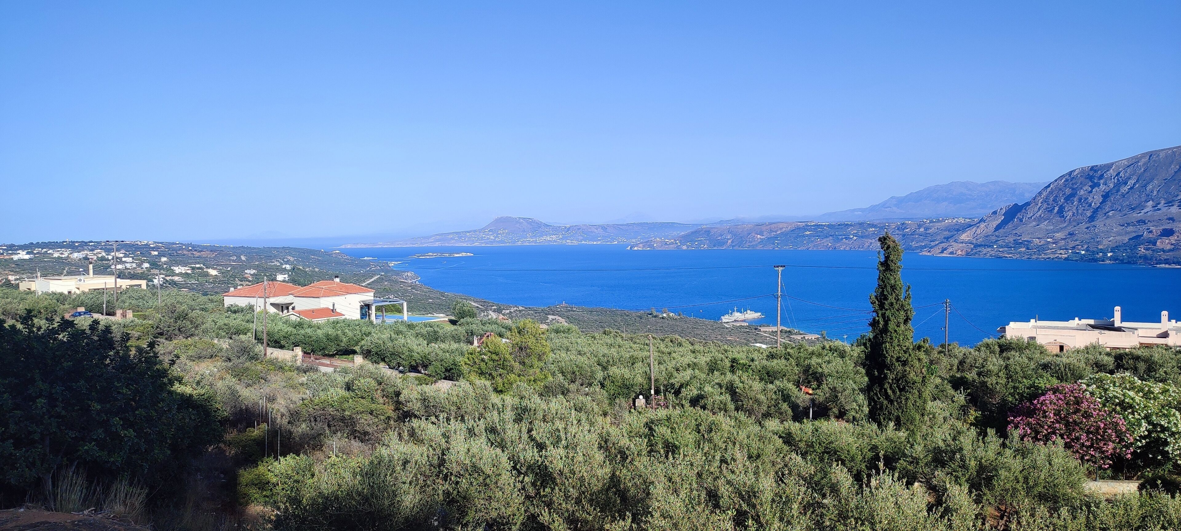 Paesaggio costiero con vista aperta sul mare, un edificio in evidenza con tetto rosso e vegetazione circostante.